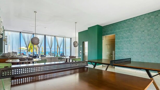 Ein moderner Essbereich mit einem langen Holztisch, Stühlen und Meerblick durch große Fenster.