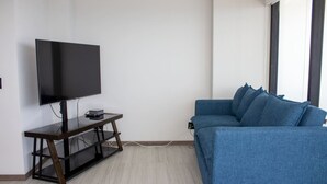 Ein Wohnzimmer mit Flachbildfernseher auf einem Schrank, einem blauen Sofa und einem Fenster mit Jalousien.