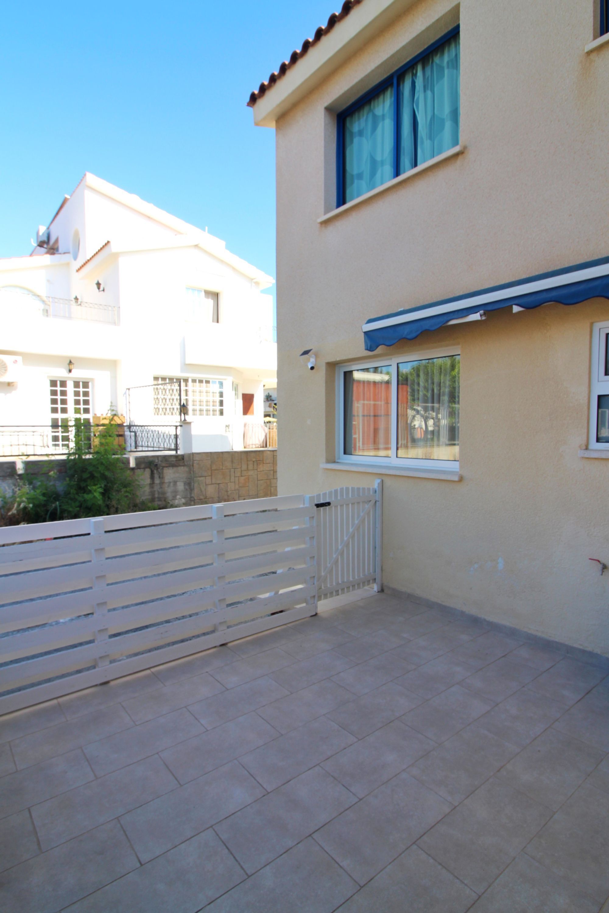 A building with a white exterior, a blue awning over a window, and a gated entrance.