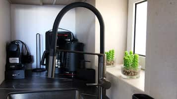 A compact kitchen with a built-in sink, a coffee machine, and a window with potted plants.