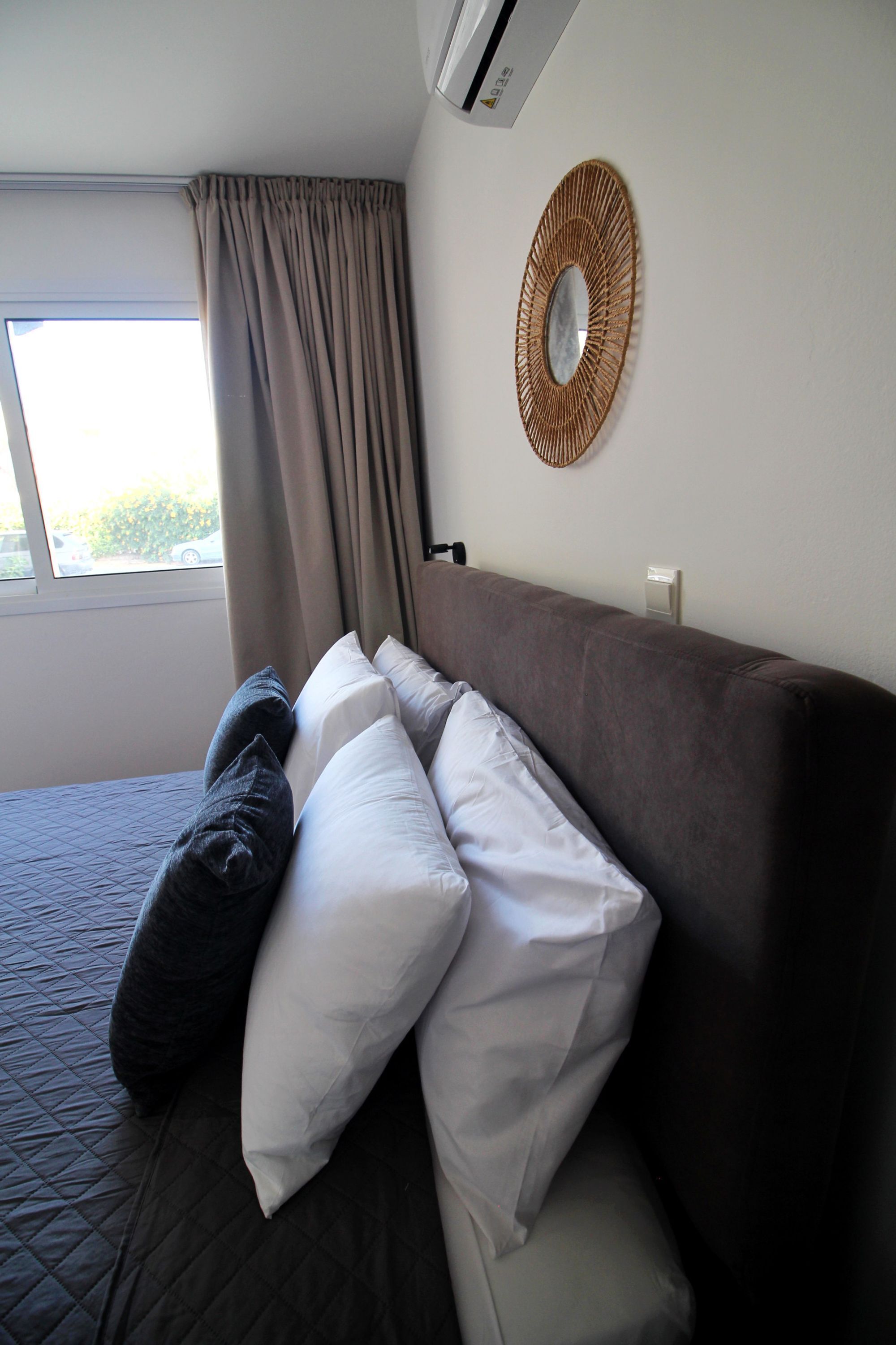 Une chambre d’hôtel avec un lit, une fenêtre avec des rideaux, un climatiseur fixé au mur et un miroir décoratif.