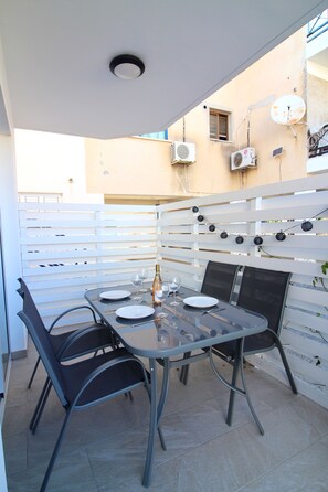 An outdoor dining area with a table set for four, surrounded by chairs, and a white fence in the background. - 106 PAP - Stay Aspri Petra Apartment (Paphos)