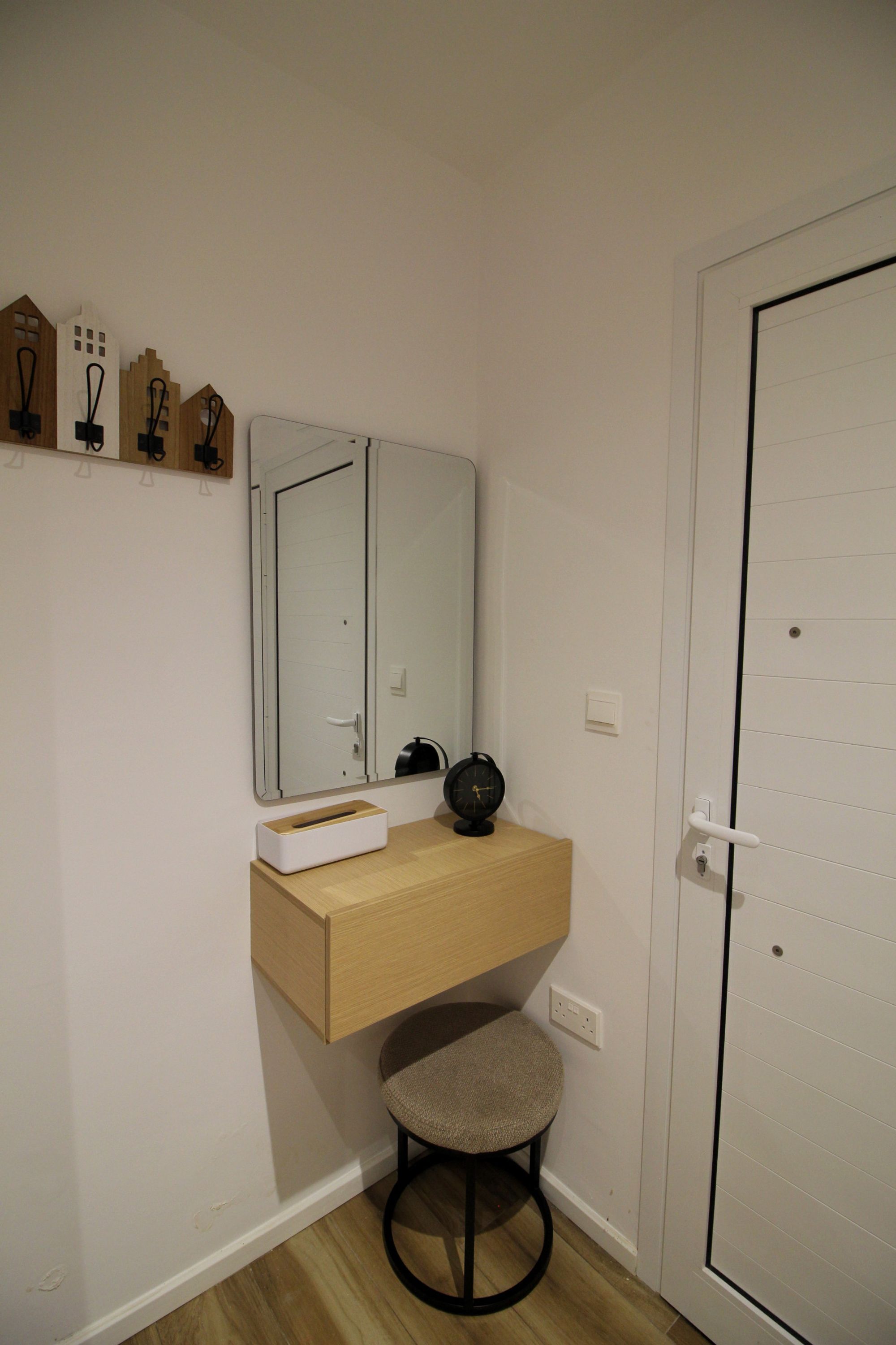A small bathroom with a wooden vanity, a round stool, a mirror, and a door with a handle.