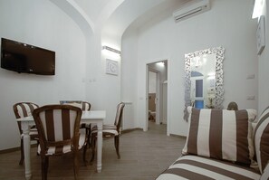 A dining area with a table and chairs, a television mounted on the wall, and a mirror with an ornate frame. - Colosseo Fori Imperiali Apartment (Rome)