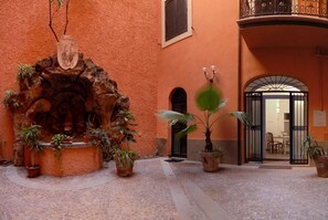 A courtyard with a fountain, potted plants, and a building entrance with a balcony. - Colosseo Fori Imperiali Apartment (Rome)