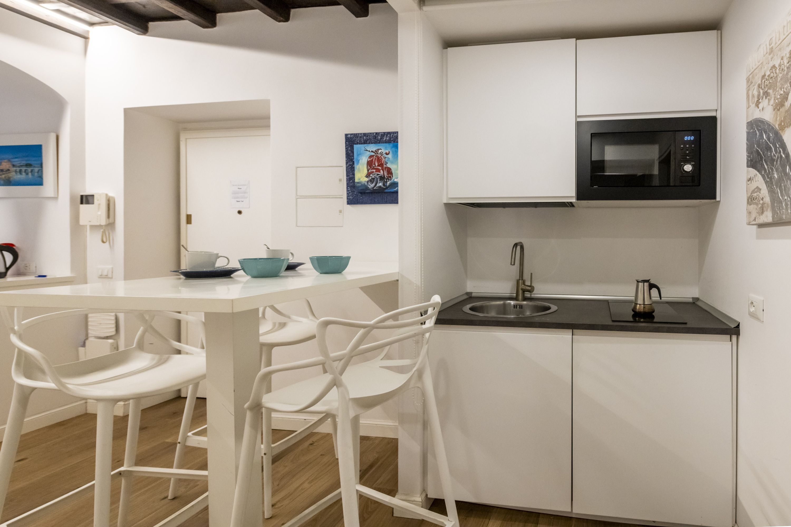 A modern kitchen with white cabinetry, a black microwave, and a stainless steel sink.