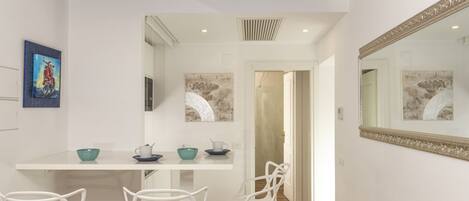 Cocina moderna con armarios blancos, una mesa de comedor y sillas. Hay un espejo grande en la pared y una obra de arte sobre la encimera.