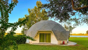 Una casa en forma de domo geodésico con una puerta corredera verde, rodeada de césped y árboles.