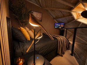 Un dormitorio acogedor con cama, lámpara, televisor y planta.