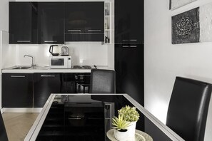 Eine moderne Küche mit schwarzen Schränken, einer Mikrowelle, einem Wasserkocher und einem Toaster. Ein Esstisch mit Stühlen und einer Topfpflanze sind ebenfalls vorhanden.