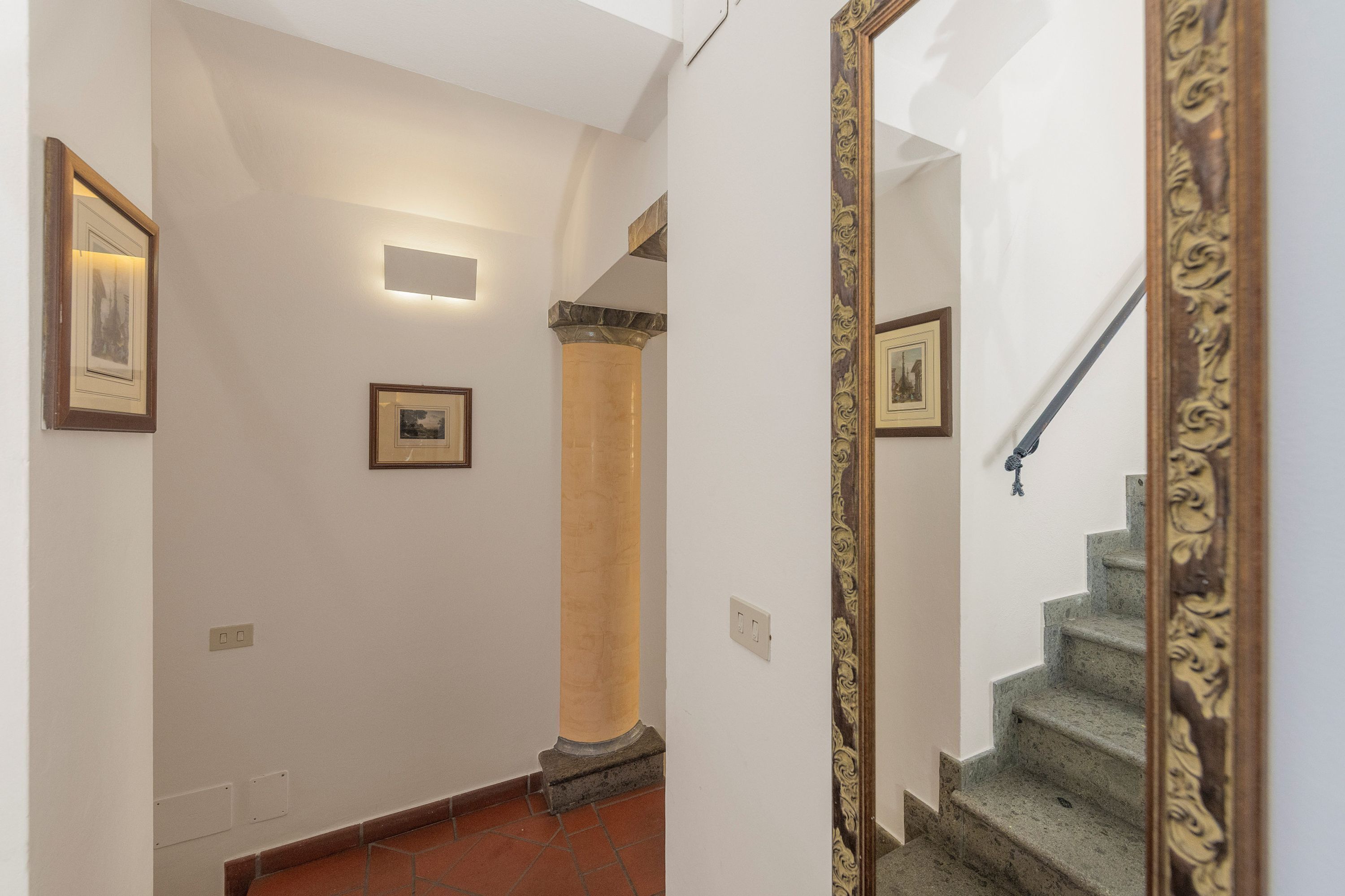 A hallway with a staircase, a mirror, and framed pictures on the walls.