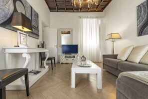 Ein modernes Wohnzimmer mit Flachbildfernseher, einem weißen Couchtisch, einem grauen Sofa und einem Esstisch mit Stühlen.