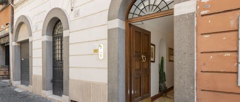 Un edificio con fachada de piedra, número 54, que presenta una puerta de madera con un panel de vidrio y una reja metálica.