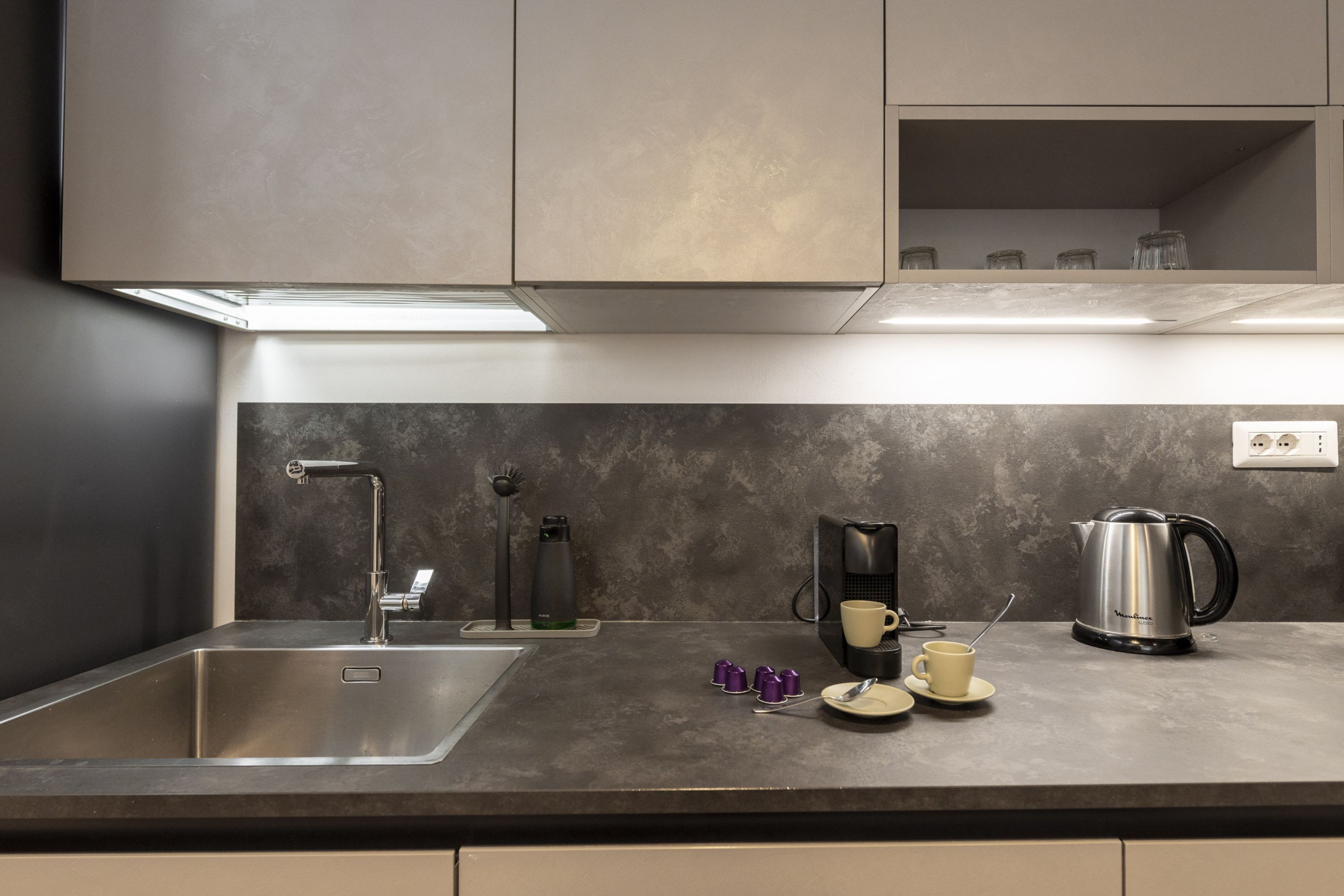 A modern kitchen with a stainless steel sink, a coffee maker, and a kettle on the counter.