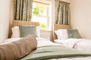 A double bed with a green blanket and two pillows, a window with floral curtains, and a radiator. - Perfect Booking Bright 2 Bed Maisonette in Bath (Bath)