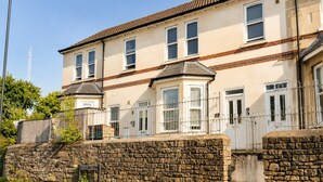A two-story building with a stone wall in front, a metal fence, and a clear sky. - Perfect Booking Bright 2 Bed Maisonette in Bath (Bath)