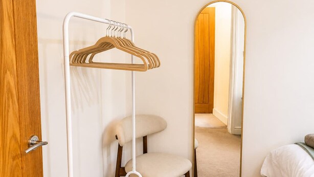 A room with a wooden door, a white wall-mounted hanger, a white chair, and a mirror reflecting a door and a hallway. - Perfect Booking Bright 2 Bed Maisonette in Bath (Bath)