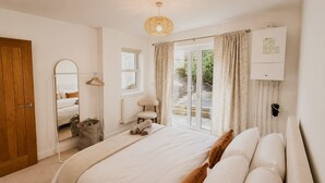 A bedroom with a bed, a mirror, a radiator, a window with curtains, and a door. - Perfect Booking Bright 2 Bed Maisonette in Bath (Bath)