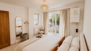 Ein Schlafzimmer mit Bett, Spiegel, Heizkörper, Fenster mit Vorhängen und einer Tür.