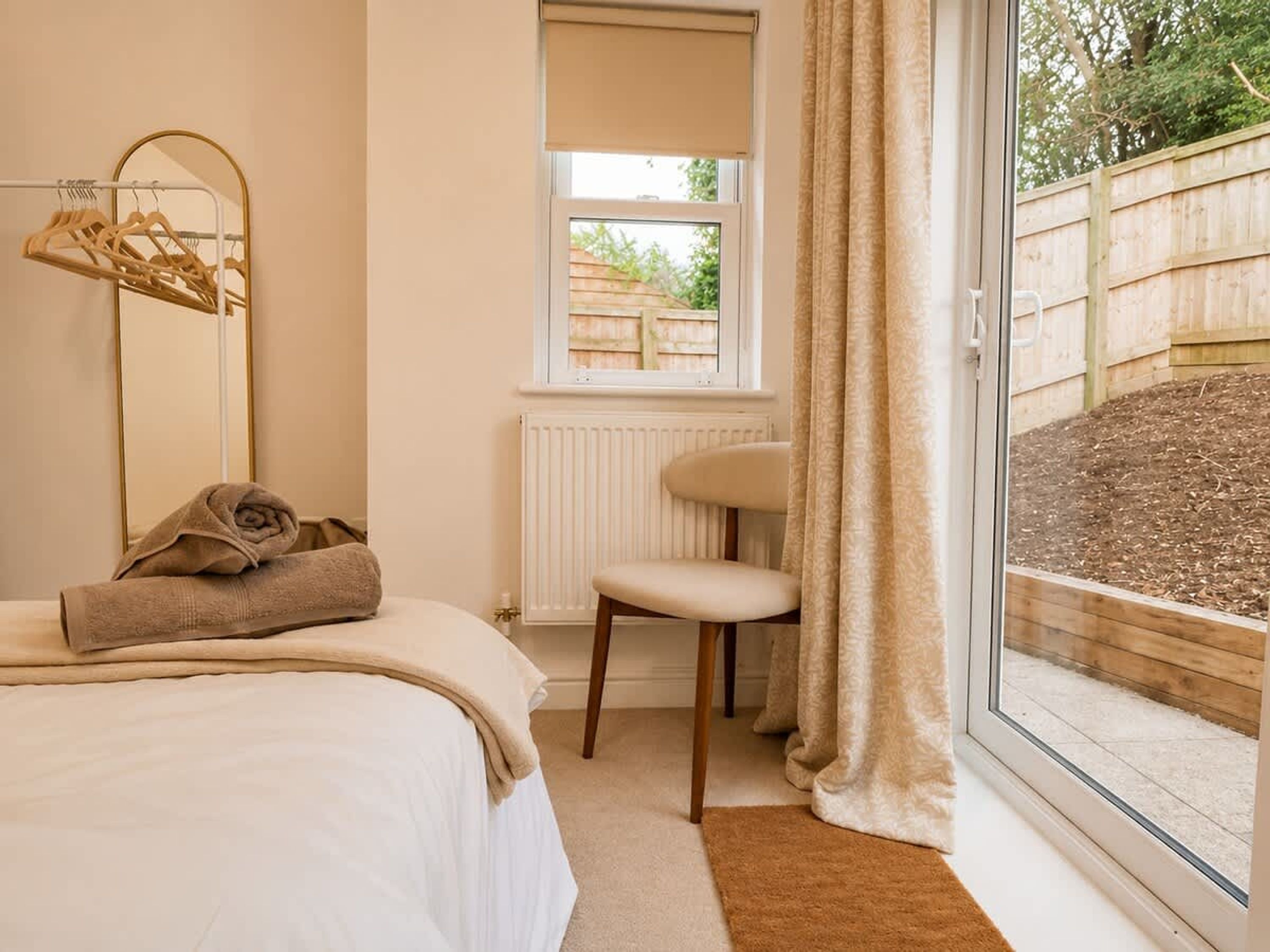 A bedroom with a bed, a chair, a window, and a view of a garden.