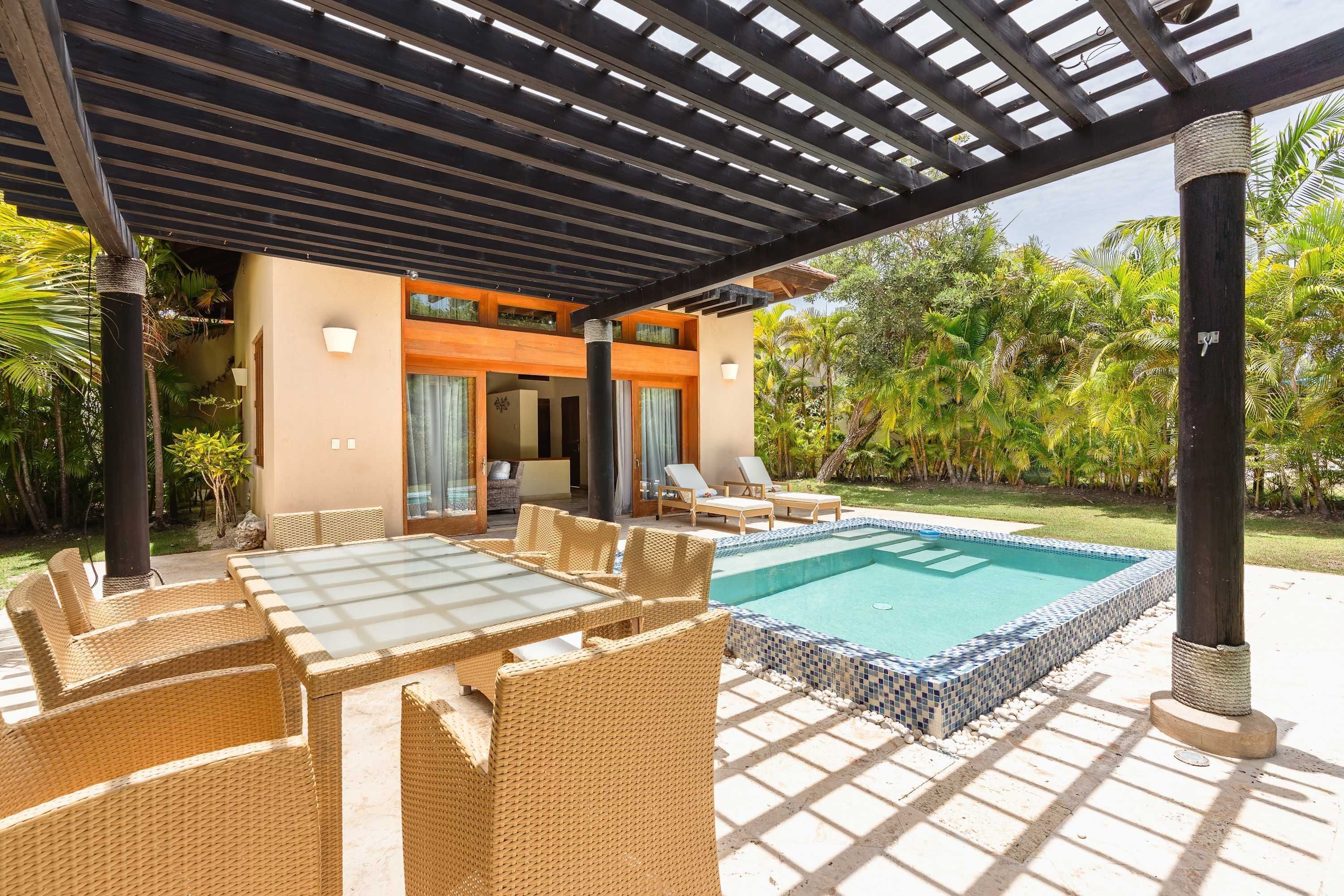 Uma área externa coberta com piscina, móveis de vime e uma pérgula de madeira.