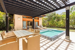 Ein überdachter Außenbereich mit Pool, Korbmöbeln und einer Holzpergola.