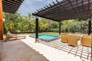 Ein überdachter Außenbereich mit Pool, Liegestühlen und Korbmöbeln.