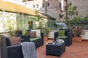 An outdoor seating area with wicker furniture, potted plants, and a view of the cityscape. - San Francesco Ripa 2 - Fornarina Oasis Cottage (Rome)