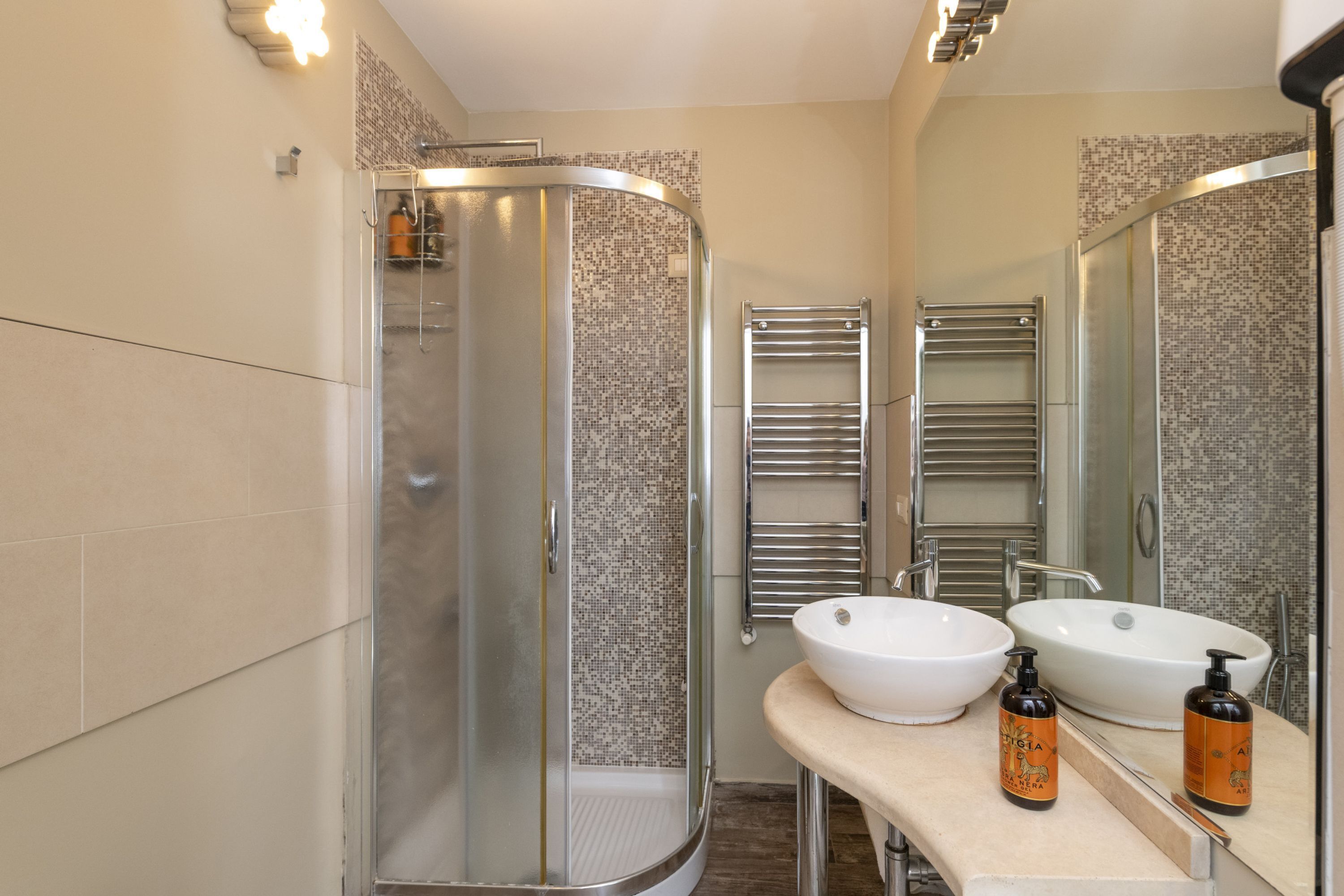Un baño moderno con ducha de vidrio, dos lavamanos y un espejo.
