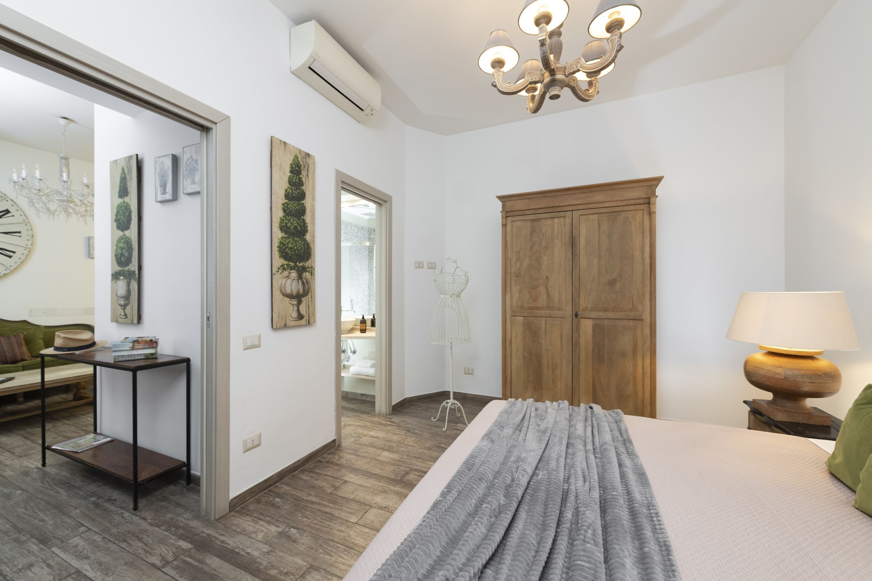 A bedroom with a bed, a wooden wardrobe, a chandelier, a bedside table, and a lamp.