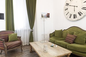 A room with a green sofa, a wooden coffee table, and a large wall clock. - San Francesco Ripa 2 - Fornarina Oasis Cottage (Rome)