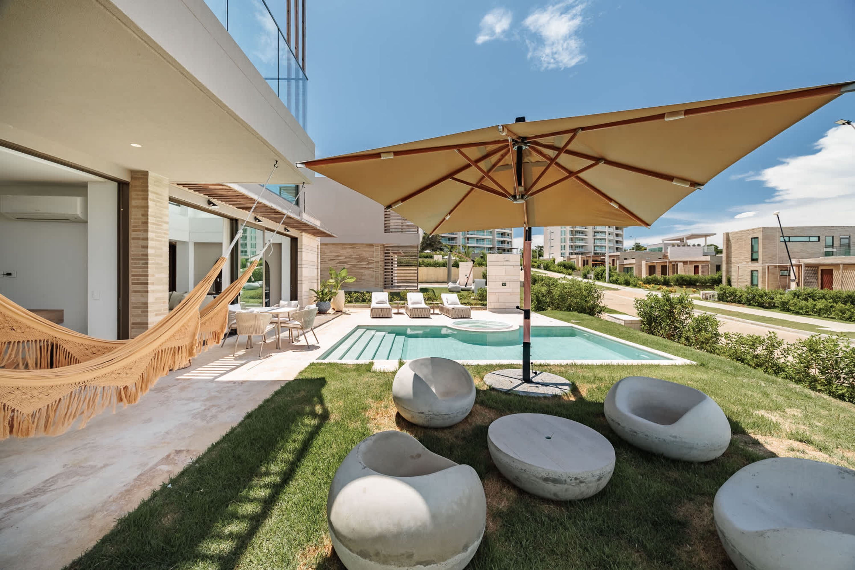 A modern outdoor pool area with lounge chairs, a hammock, and a large umbrella.