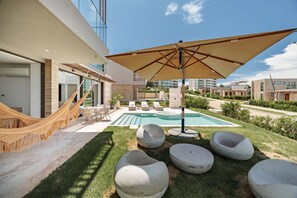 A modern outdoor pool area with lounge chairs, a hammock, and a large umbrella.