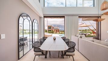 A modern dining area with a long table, black wicker chairs, and a view of a pool and building.