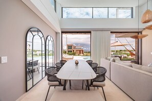A modern dining area with a long table, black wicker chairs, and a view of a pool and building.