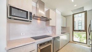 A modern kitchen with a built-in microwave, oven, dishwasher, and a large window offering a view of greenery. - Modern 4 Bedroom Villa With Tropical Vibes in Baru (Cartagena)