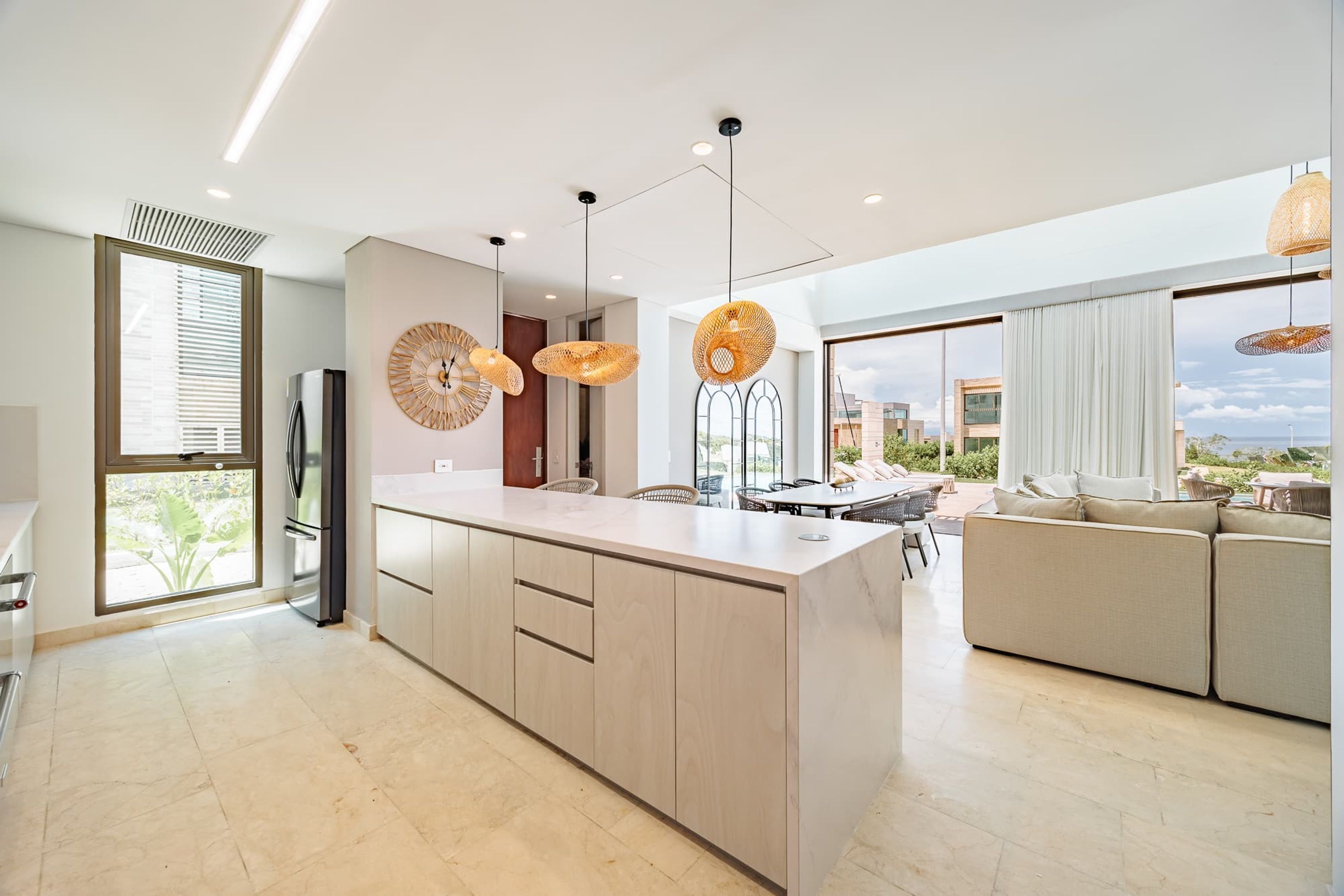 A modern kitchen with a central island, pendant lights, and a view to the outside.