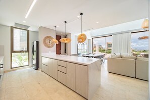 A modern kitchen with a central island, pendant lights, and a view to the outside.