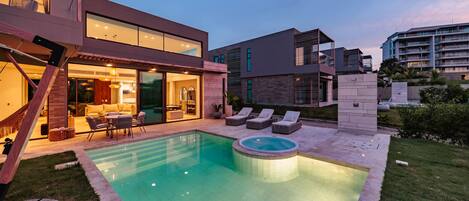 A modern house with a swimming pool, outdoor seating, and a well-lit patio area.
