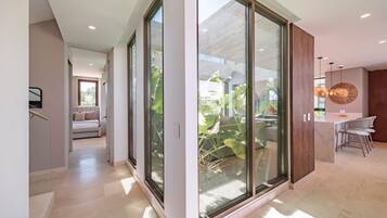 A modern interior with a glass door leading to a balcony, a dining area with a round table and chairs, and a bedroom with a bed and a window.