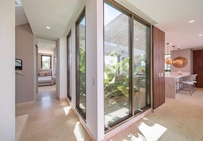 A modern interior with a glass door leading to a balcony, a dining area with a round table and chairs, and a bedroom with a bed and a window.