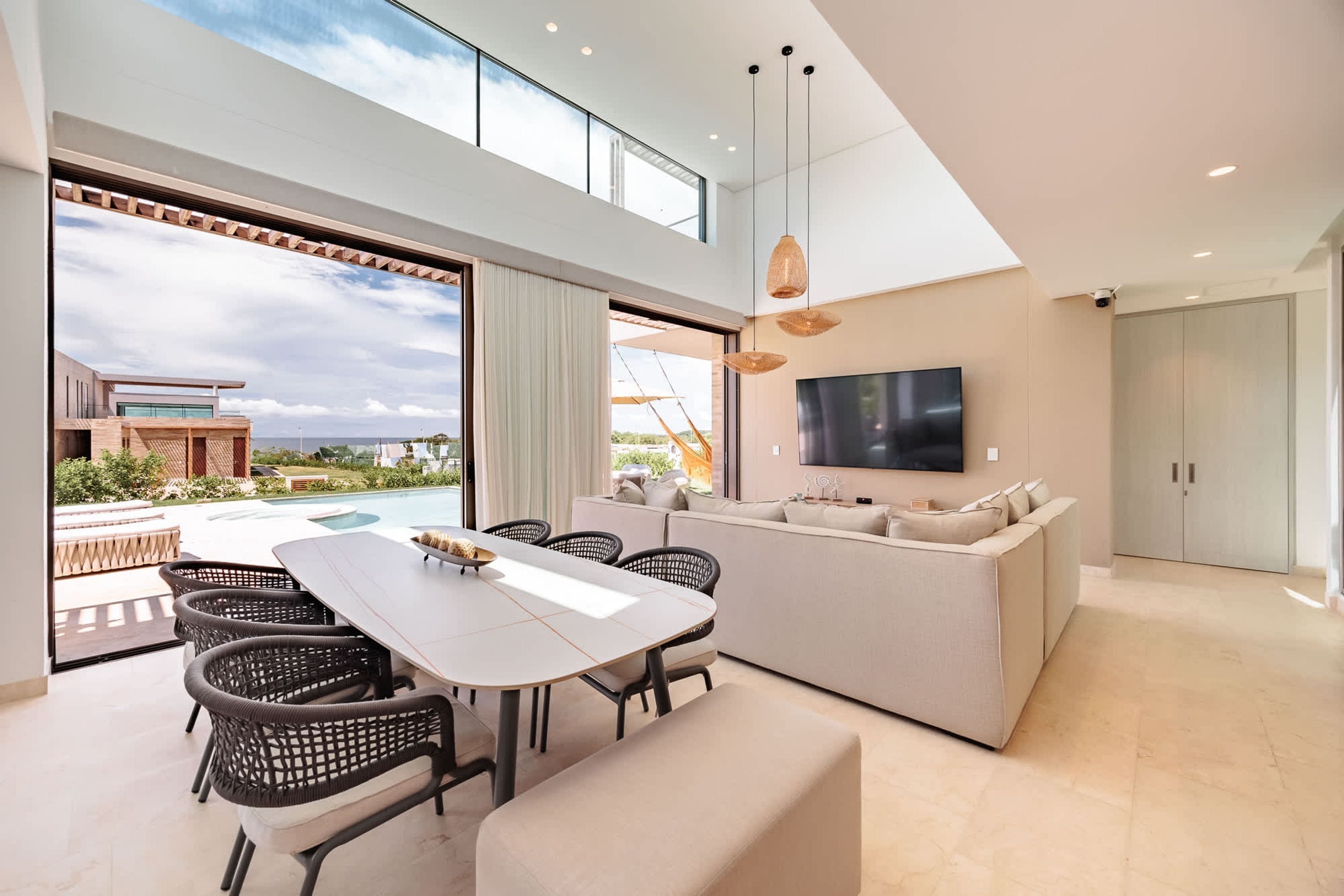 A modern living room with a large TV, a dining area with a table and chairs, and a sofa.