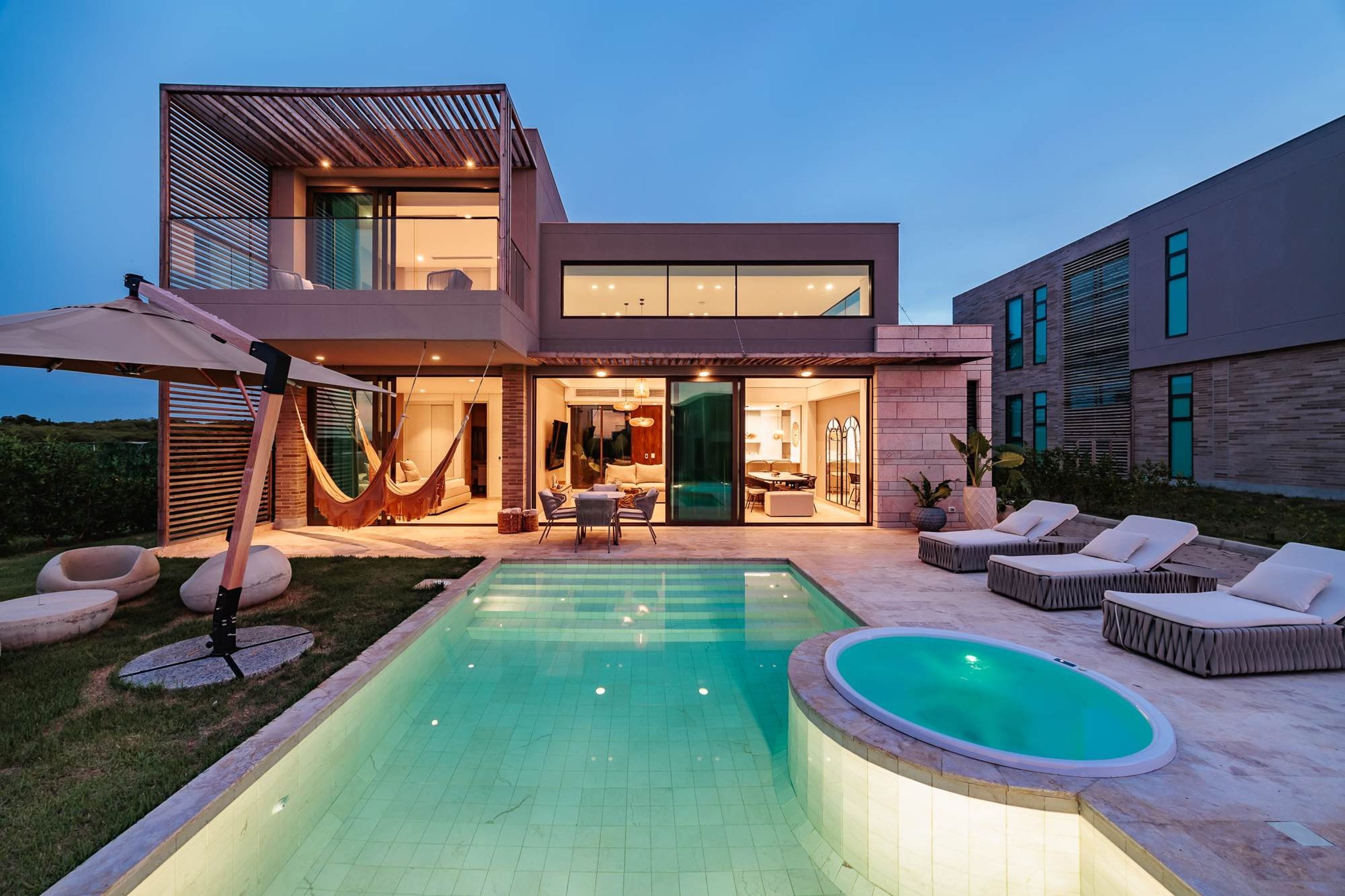 A modern two-story house with a swimming pool, outdoor seating, and a hammock.
