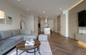 Ein modernes Wohnzimmer mit einem grauen Sofa, einem runden Couchtisch und einem Flachbildfernseher.