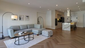 Ein modernes Wohnzimmer mit grauem Sofa, einem runden Couchtisch und einem weißen Hocker.