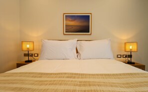 Ein Hotelzimmer mit Bett, zwei Nachttischlampen, einem Wandbild und einer Steckdose.