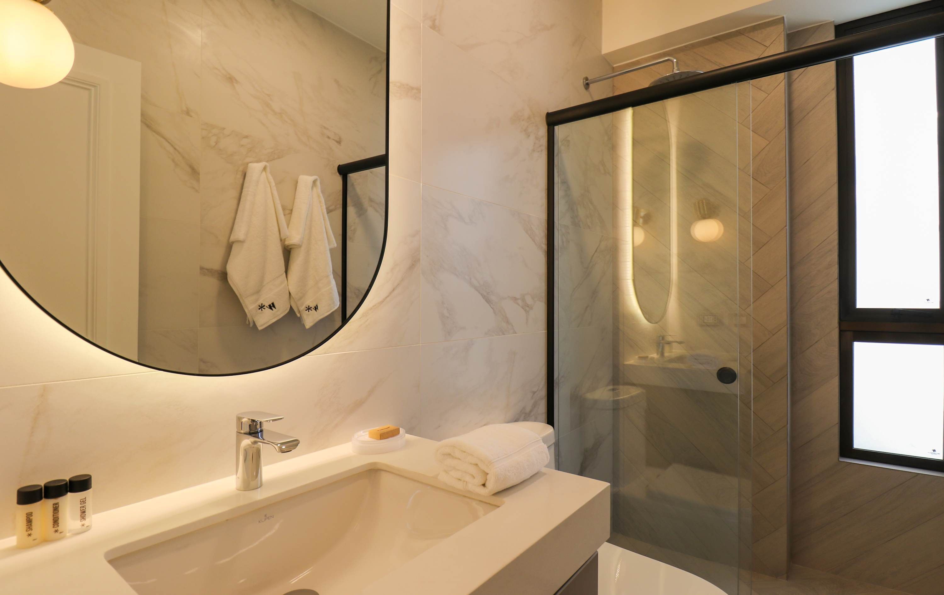 A modern bathroom with a marble vanity, a glass shower enclosure, and a large mirror.