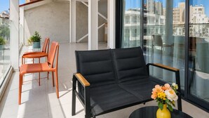 Uma varanda moderna com um sofá, cadeiras e uma mesa com um vaso de flores.