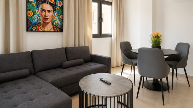 Uma sala de estar moderna com um sofá modular cinza, uma mesa de centro redonda e um espaço de jantar com uma mesa pequena e quatro cadeiras.