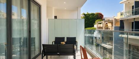 A balcony with a glass railing, a table, two chairs, and a potted plant.